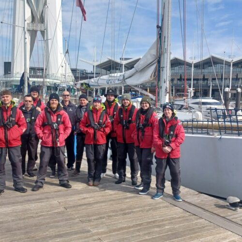 Group stood on pontoon in front of challenger in wet weather clothes and life jackets